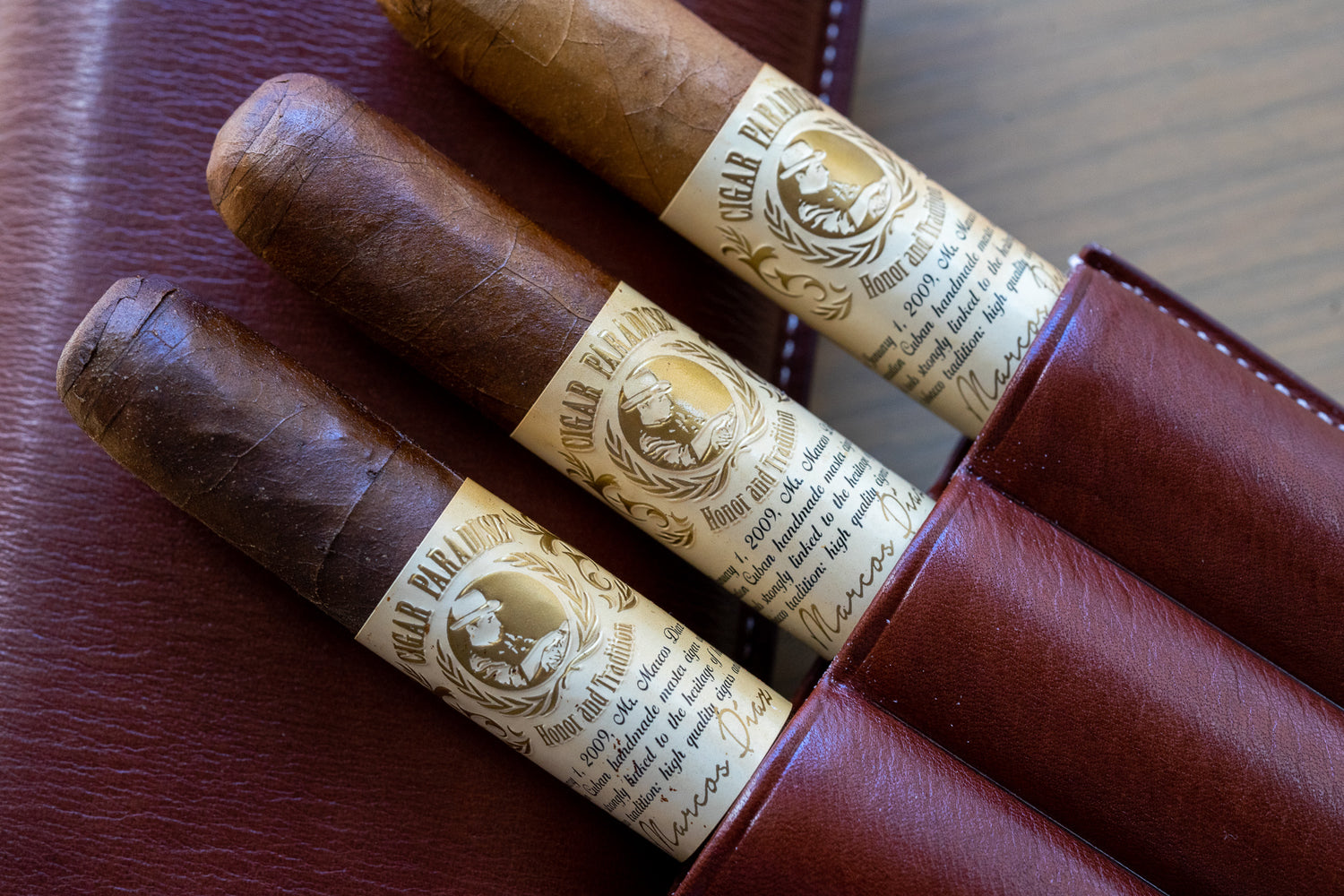 Three handcrafted Cigar Paradise House Blend cigars with original branded bands, displayed in a brown leather cigar holder.